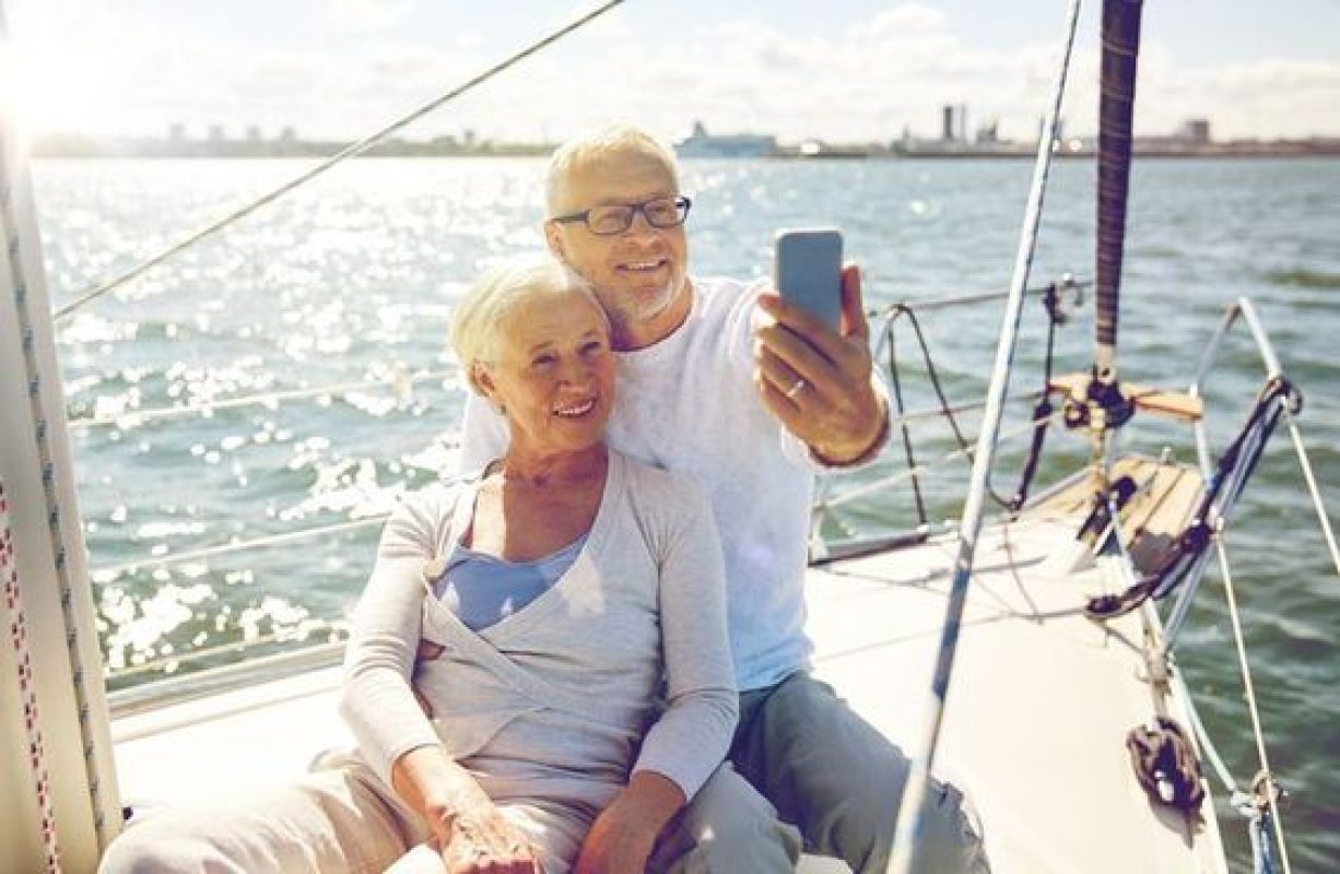 62581196 - sailing, technology, tourism, travel and people concept - happy senior couple with smartphone taking selfie on sail boat or yacht deck floating in sea